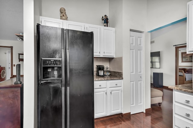 kitchen featuring dark stone counters, dark wood-type flooring, black fridge, white cabinetry, and backsplash