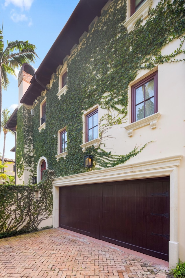 view of home's exterior with a garage, decorative driveway, a chimney, and stucco siding