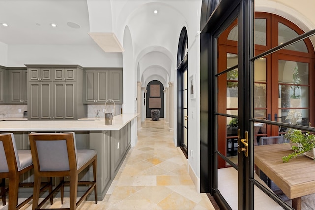 kitchen with arched walkways, a breakfast bar, light countertops, decorative backsplash, and gray cabinetry