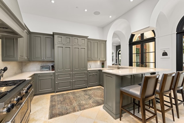 kitchen featuring a peninsula, a breakfast bar, light countertops, gray cabinets, and tasteful backsplash