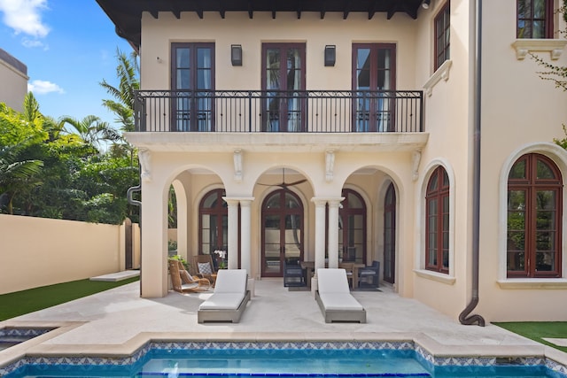 rear view of property with french doors, stucco siding, a patio area, a balcony, and an outdoor pool