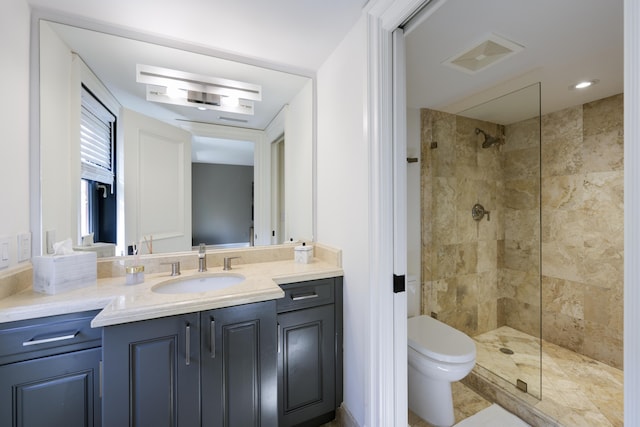 bathroom with toilet, visible vents, tiled shower, and vanity