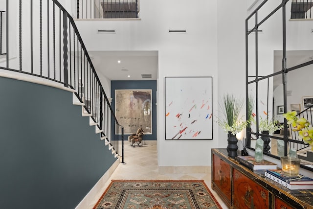 tiled entrance foyer featuring visible vents, a towering ceiling, and stairs