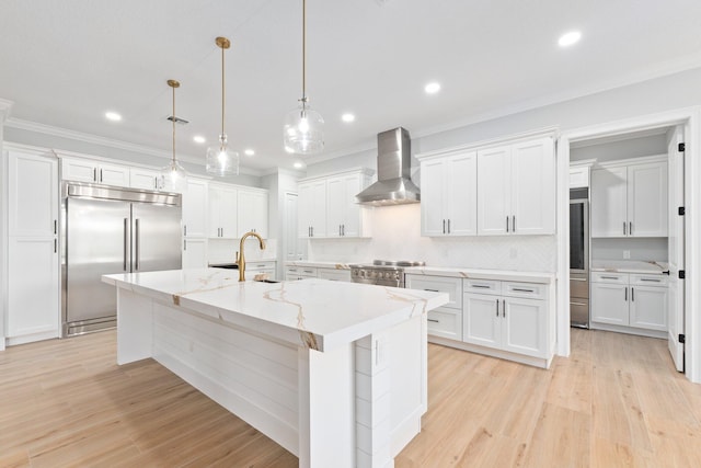 kitchen featuring wall chimney range hood, a kitchen island with sink, white cabinetry, and premium appliances