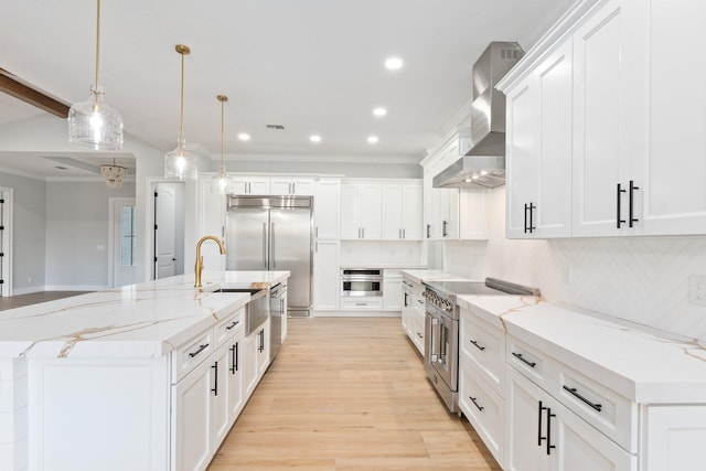 kitchen featuring premium appliances, decorative light fixtures, a large island, white cabinets, and wall chimney exhaust hood