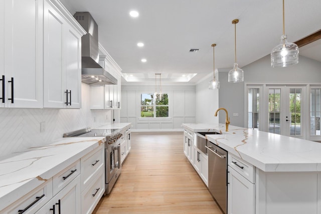 kitchen featuring white cabinets, appliances with stainless steel finishes, a large island, wall chimney exhaust hood, and pendant lighting