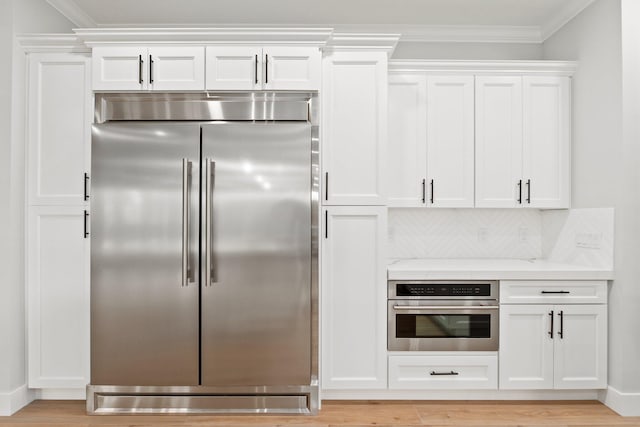 kitchen with stainless steel appliances, white cabinets, crown molding, and light stone counters