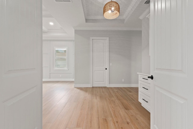 spare room with light wood-type flooring, a tray ceiling, crown molding, and baseboards