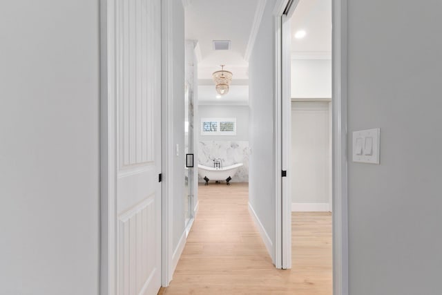 hall with light wood-type flooring, visible vents, ornamental molding, and baseboards