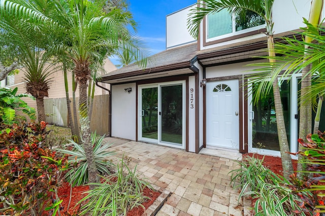 property entrance featuring a patio, roof with shingles, fence, and stucco siding