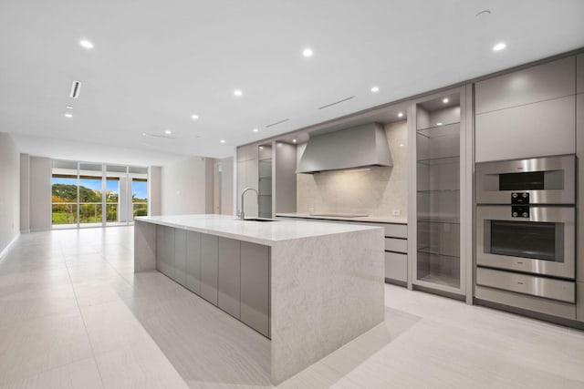 kitchen with wall chimney exhaust hood, modern cabinets, gray cabinets, a large island with sink, and a sink