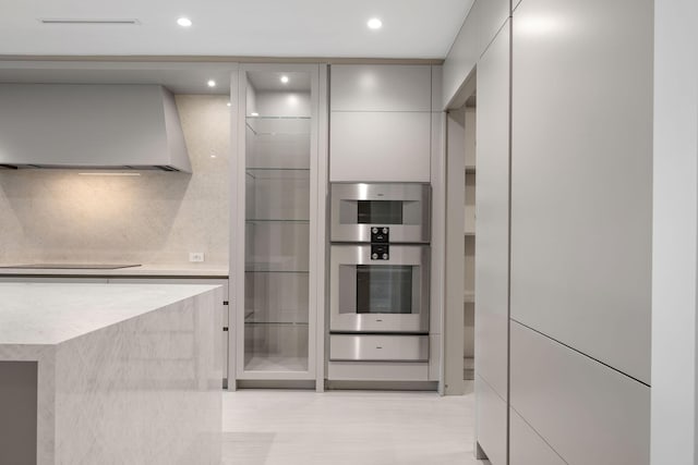 kitchen featuring gray cabinets, light countertops, stainless steel double oven, wall chimney range hood, and modern cabinets