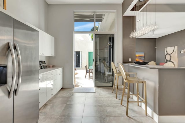 kitchen with stainless steel refrigerator with ice dispenser, a breakfast bar area, light countertops, white cabinets, and a peninsula