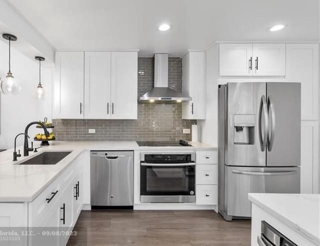 kitchen featuring stainless steel appliances, dark wood-type flooring, a sink, and wall chimney range hood