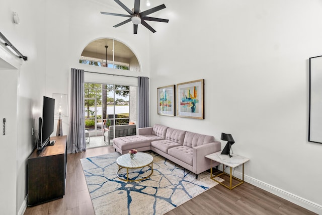 living area with ceiling fan, a barn door, a high ceiling, wood finished floors, and baseboards