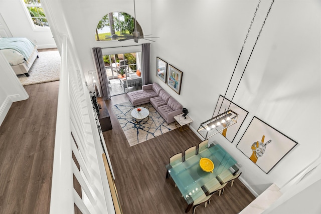 living area with a towering ceiling, ceiling fan, baseboards, and wood finished floors