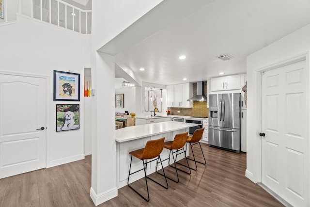 kitchen with a peninsula, a breakfast bar, visible vents, wall chimney range hood, and stainless steel fridge