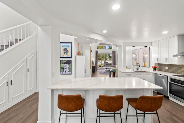 kitchen featuring tasteful backsplash, appliances with stainless steel finishes, a sink, wood finished floors, and a peninsula