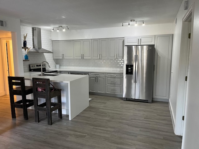 kitchen with stainless steel fridge with ice dispenser, wall chimney exhaust hood, a breakfast bar area, light countertops, and a sink