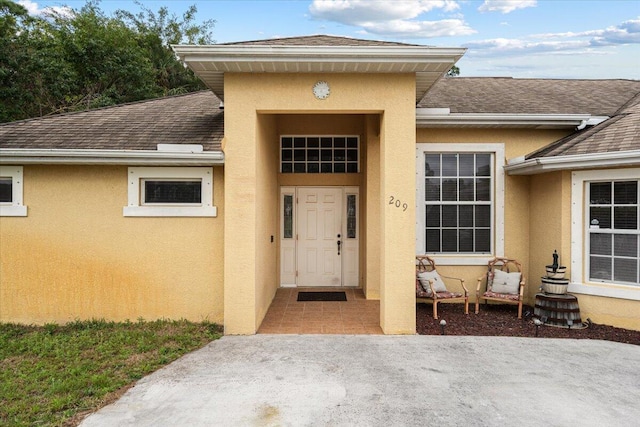 view of exterior entry with a patio area, roof with shingles, and stucco siding