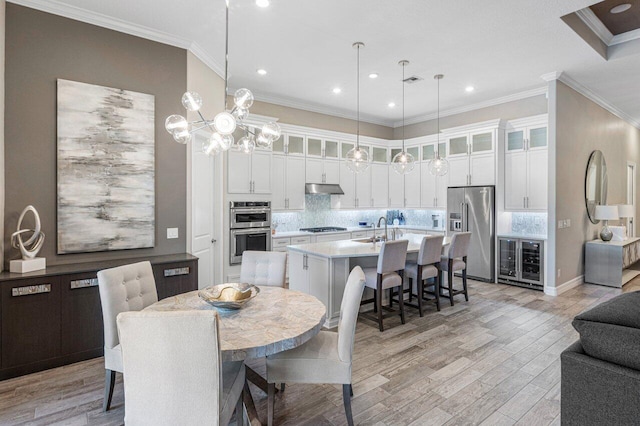 kitchen with light countertops, appliances with stainless steel finishes, glass insert cabinets, an island with sink, and under cabinet range hood