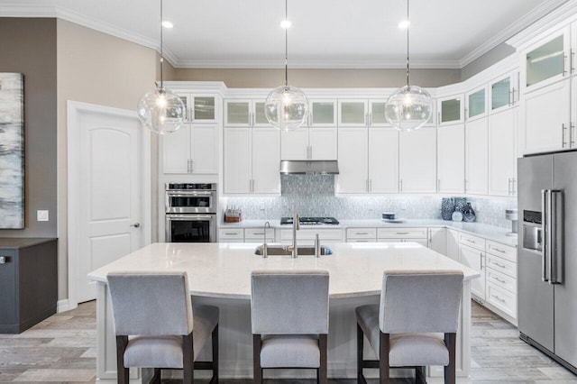 kitchen featuring stainless steel appliances, a center island with sink, glass insert cabinets, and under cabinet range hood