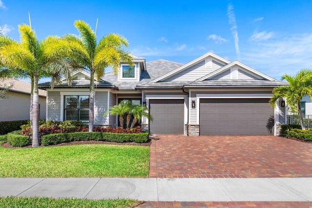 view of front facade featuring a garage, stone siding, decorative driveway, and a front yard