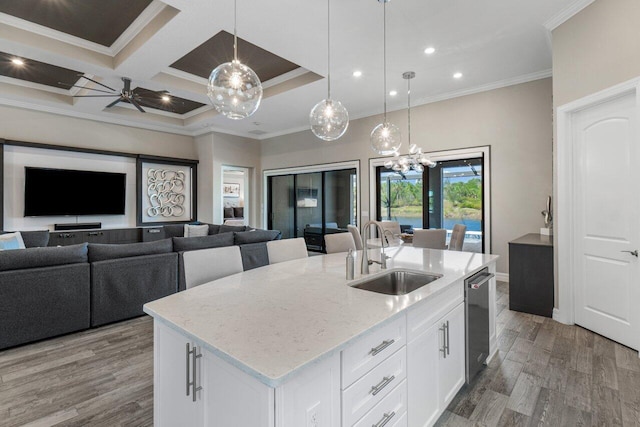 kitchen featuring white cabinets, an island with sink, open floor plan, hanging light fixtures, and a sink