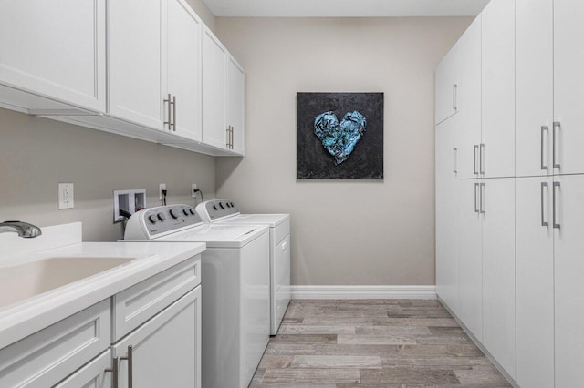 laundry room featuring cabinet space, light wood-style flooring, washing machine and dryer, a sink, and baseboards