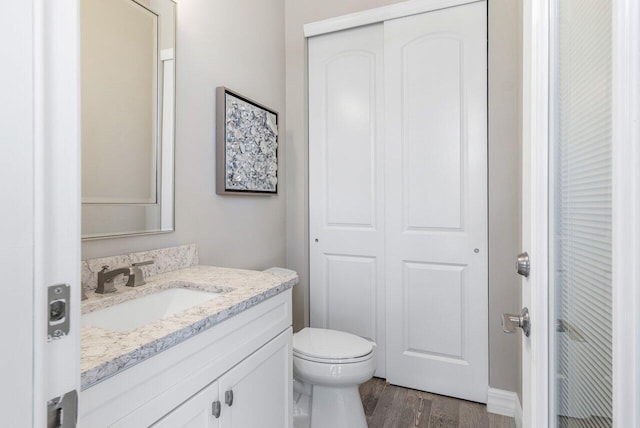 bathroom featuring toilet, a closet, wood finished floors, and vanity