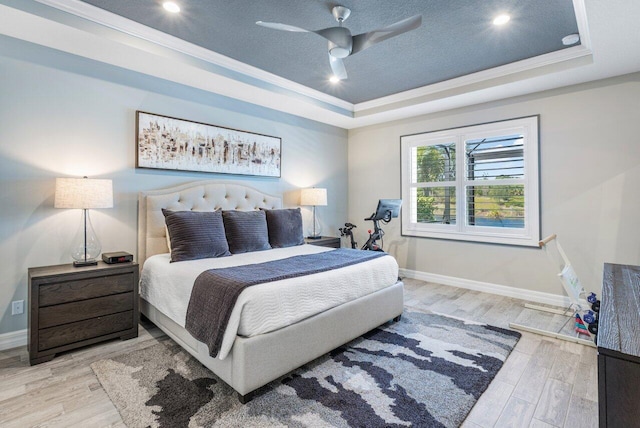 bedroom with baseboards, a raised ceiling, light wood-style flooring, ornamental molding, and a textured ceiling