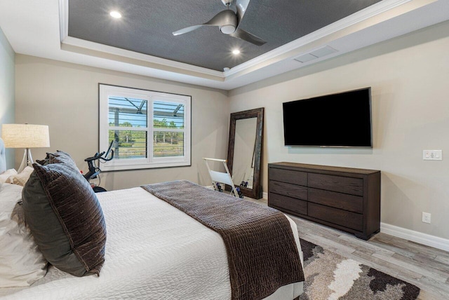 bedroom featuring visible vents, a tray ceiling, light wood-style flooring, and baseboards