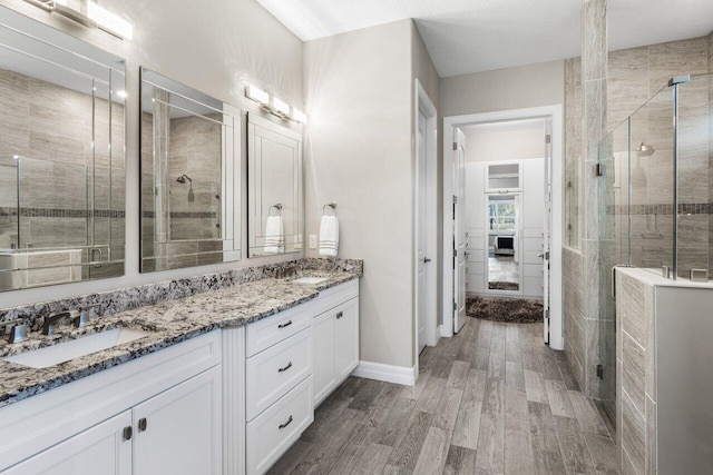 full bathroom with double vanity, wood finished floors, a sink, and a shower stall