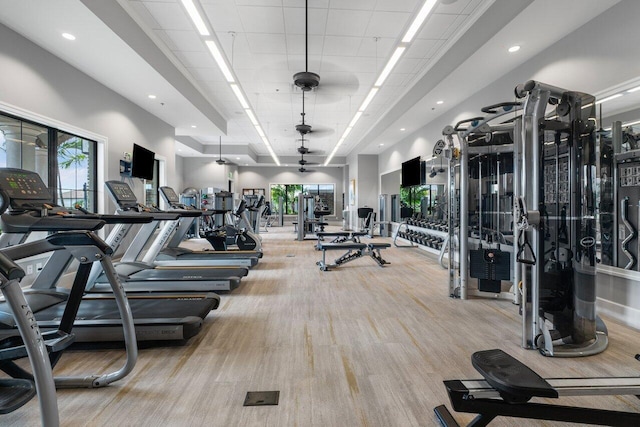 workout area with recessed lighting, light wood-type flooring, a raised ceiling, and a healthy amount of sunlight