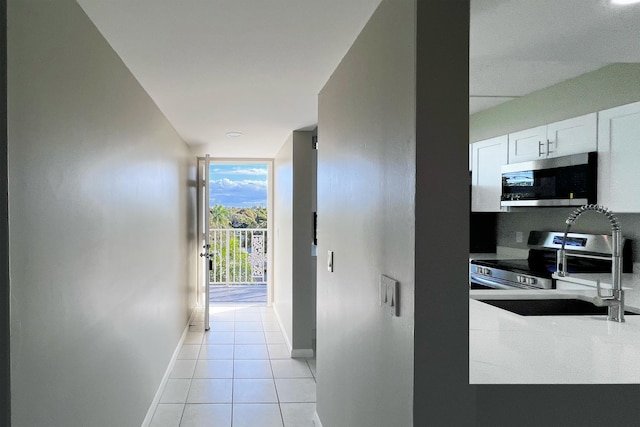 hall featuring floor to ceiling windows, light tile patterned flooring, a sink, and baseboards