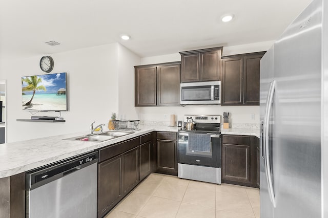 kitchen with light tile patterned floors, dark brown cabinetry, stainless steel appliances, a peninsula, and a sink