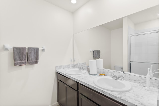 bathroom with double vanity, an enclosed shower, a sink, and toilet