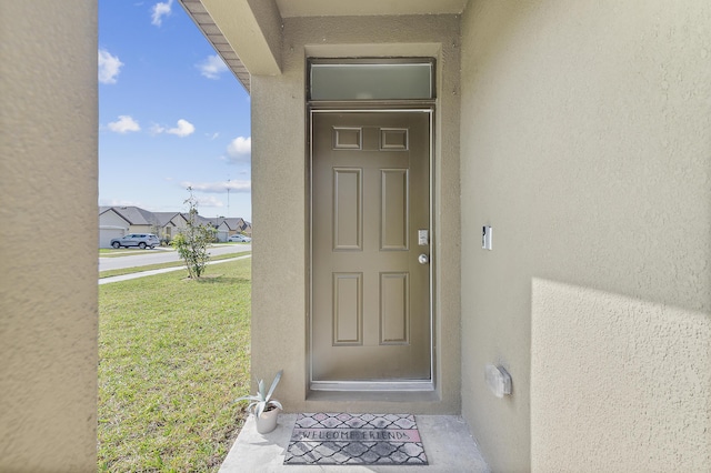 view of exterior entry featuring a lawn and stucco siding