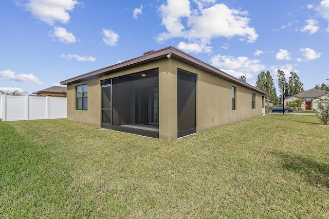 back of property featuring a sunroom, stucco siding, a lawn, and fence