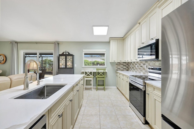 kitchen featuring stainless steel appliances, cream cabinets, a sink, and light countertops