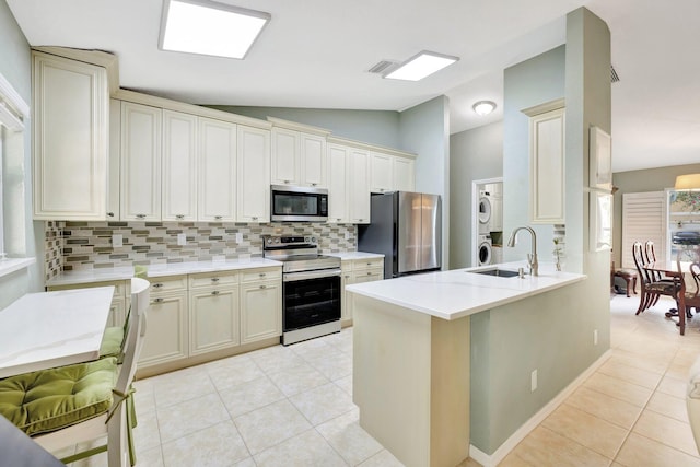 kitchen with stainless steel appliances, stacked washer and dryer, light countertops, light tile patterned flooring, and a sink