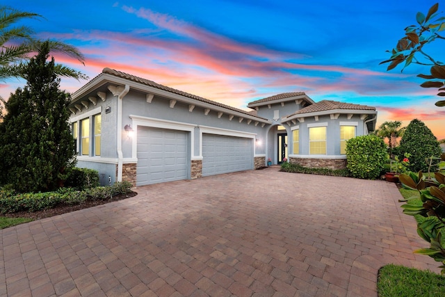 mediterranean / spanish-style home featuring a garage, stone siding, decorative driveway, and stucco siding