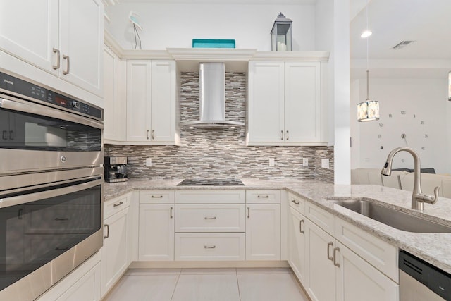 kitchen with light stone counters, appliances with stainless steel finishes, wall chimney range hood, pendant lighting, and a sink