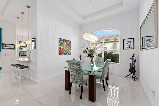 dining area with light tile patterned floors, baseboards, and a raised ceiling