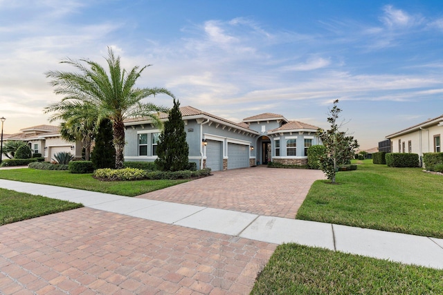 view of front of home with a tiled roof, an attached garage, decorative driveway, a front lawn, and stucco siding