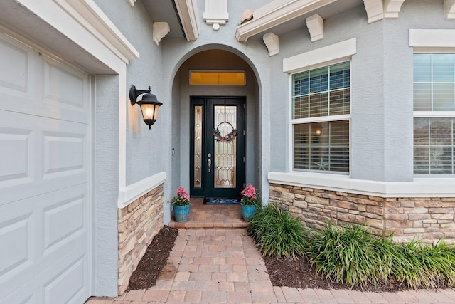 entrance to property featuring a garage, stone siding, and stucco siding