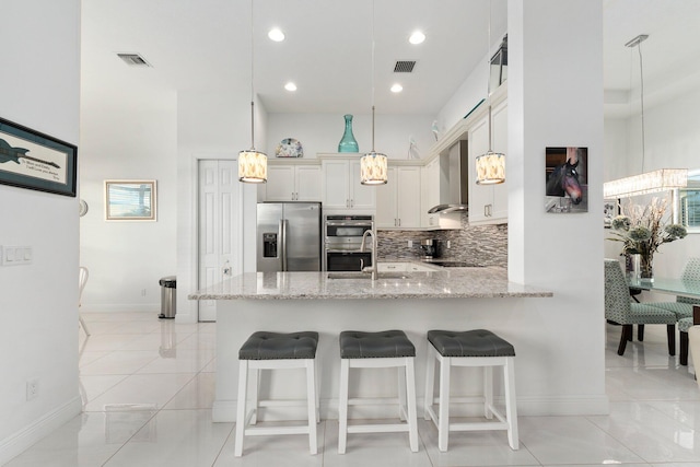 kitchen featuring decorative backsplash, wall chimney exhaust hood, appliances with stainless steel finishes, hanging light fixtures, and a peninsula