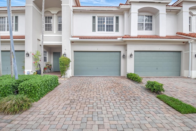 townhome / multi-family property featuring an attached garage, stucco siding, decorative driveway, and a tiled roof