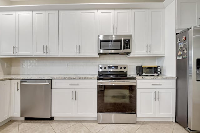 kitchen with light tile patterned floors, decorative backsplash, appliances with stainless steel finishes, white cabinets, and light stone countertops