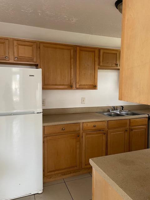 kitchen featuring freestanding refrigerator, light countertops, a sink, and light tile patterned floors